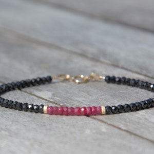 Könnte beinhalten: Ein schwarzes und rotes Perlenarmband mit einem goldenen Verschluss. Das Armband besteht aus schwarzen Spinellperlen und roten Rubinperlen.