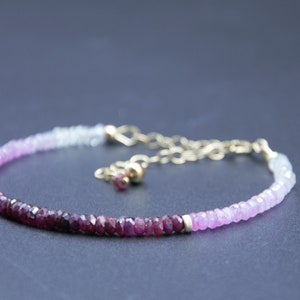 Könnte beinhalten: Ein zartes Armband aus einer goldenen Kette mit einem Farbverlauf aus rosa und roten Edelsteinperlen. Die Perlen sind facettiert und haben einen dezenten Schimmer.