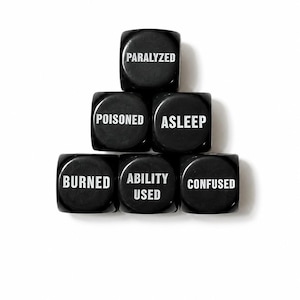 May include: A set of six black six-sided dice arranged in a pyramid formation. Each die face features white text including the words PARALYZED, POISONED, ASLEEP, BURNED, ABILITY USED, and CONFUSED, representing various status effects for gaming.