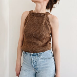 May include: A brown knitted halter top with a ribbed texture. The top features a high neckline and a sleeveless design. The garment is made of a soft, textured yarn, suitable for casual wear.