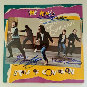Puede incluir: Una portada de álbum de vinilo vintage con una banda de cuatro hombres vestidos de negro y blanco. La portada del álbum se titula "The Kinks State of Confusion." La portada del álbum está firmada por los miembros de la banda.
