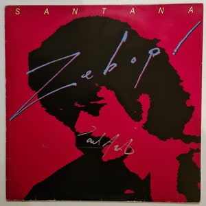 Puede incluir: Una portada de disco de vinilo rojo con el t&iacute;tulo "Zebop!" en letras azules y negras. La portada presenta una silueta negra de la cabeza y los hombros de una persona. El &aacute;lbum es de Santana.
