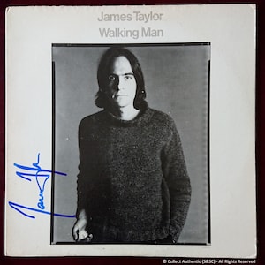 Op de afbeelding: Een zwart-witfoto van James Taylor op de hoes van zijn album "Walking Man". De albumhoes toont een close-up van James Taylor die een donkere trui draagt en recht in de camera kijkt. De albumtitel "Walking Man" is in witte tekst boven de foto gedrukt.