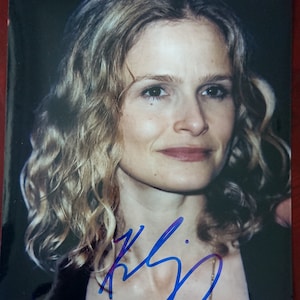 Puede incluir: Una foto de primer plano de una mujer con cabello rubio y ojos azules. Ella est&aacute; sonriendo y mirando a la c&aacute;mara. Su firma est&aacute; escrita en tinta azul debajo de su imagen.