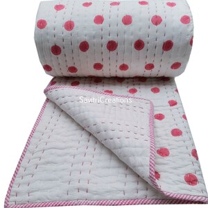 May include: White cotton quilt with a pink polka dot pattern and pink and white striped border. The quilt is rolled up and folded in half.