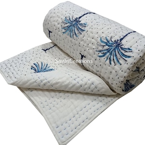 May include: White cotton quilt with a blue and white floral pattern. The quilt is rolled up and has a white background with blue stitching.
