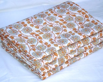 Puede incluir: Edredón blanco plegado con un estampado floral repetido en amarillo, naranja y azul. Las flores están conectadas por tallos y hojas marrones. El edredón está apilado, mostrando las costuras detalladas.