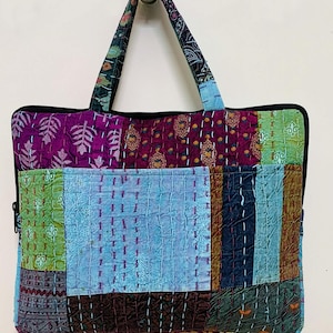 May include: A patchwork laptop bag with a blue, green, purple, and brown color scheme. The bag has a zipper closure and two fabric handles.