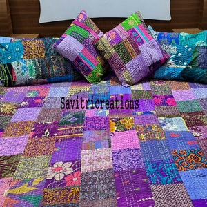 Może przedstawiać: Pikowana kołdra i trzy pasujące poduszki. Kołdra i poduszki mają różne tkaniny w odcieniach fioletu, różu, zieleni i niebieskiego. Kołdra jest prostokątna i zakrywa łóżko. Poduszki są kwadratowe.