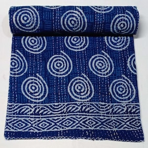 Op de afbeelding: Een blauwe en witte kantha-deken met een draaiend patroon. De deken is met de hand gestikt en heeft een decoratieve rand.