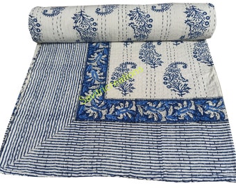 May include: A white and blue patterned quilt with a rolled-up section. The quilt features a repeating floral design in blue, with a striped border and a floral border. The stitching is visible.