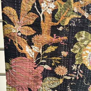 Op de afbeelding: Zwarte kantha-deken met een bloemenpatroon in tinten bruin, roze en wit. De deken is gemaakt van katoen en heeft een handgestikt ontwerp.