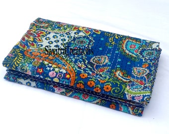 May include: A folded blue and white kantha quilt with a paisley pattern. The quilt is made of cotton and has a hand-stitched design.