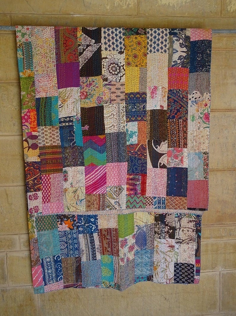 K&ouml;nnte beinhalten: Ein farbenfroher Patchwork-Deckenbezug aus verschiedenen Stoffen mit unterschiedlichen Mustern und Farben. Der Bezug besteht aus vielen kleinen Quadraten, die zusammengen&auml;ht wurden, um ein gr&ouml;&szlig;eres Design zu schaffen. Der Bezug h&auml;ngt an einer Wand.