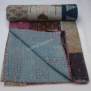 Peut inclure: Une courtepointe patchwork dans des tons de bleu, marron et rose. La courtepointe est faite de différents tissus et présente un design cousu à la main. La courtepointe est enroulée et pliée sur l'image. Le texte "Savitri Creations" est visible sur la courtepointe.