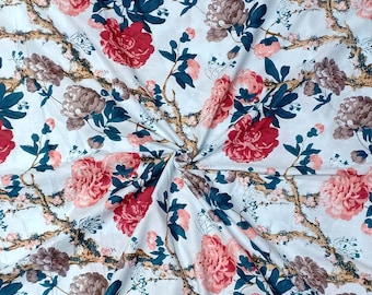 May include: White fabric with a floral print featuring pink, red, and brown flowers with green leaves. The fabric is folded in a spiral pattern.