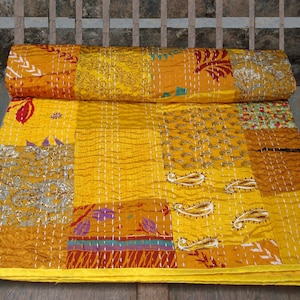 May include: A yellow, orange, and brown patchwork quilt with a kantha stitch pattern. The quilt is made of recycled saris and is hand-stitched.