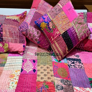 Könnte beinhalten: Eine rosafarbene und violette Patchwork-Decke mit verschiedenen Mustern und Texturen. Die Decke besteht aus Quadraten und Rechtecken aus verschiedenen Stoffen und ist mit Stickereien und Nähten verziert. Die Decke ist auf einem Bett mit passenden Kissenbezügen drapiert.