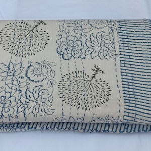 May include: A white cotton quilt with a blue and brown floral print. The quilt is folded in half and has a blue and white striped border.