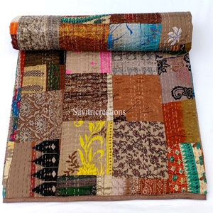 May include: A patchwork quilt in shades of brown, orange, and green, featuring diverse fabric patterns. Hand-stitched with white thread, it has a rolled top section. The text "Savitricreations" is visible on the quilt's surface.