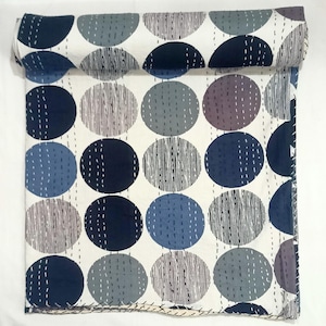 May include: A folded textile featuring a repeating pattern of large circles in shades of navy blue, light blue, and grey against a white background. The circles are accented with vertical white dashed stitching lines throughout the fabric surface.