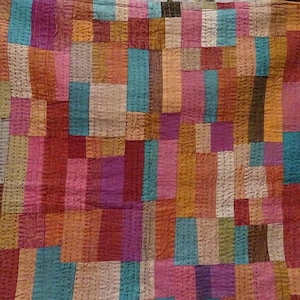 May include: A patchwork quilt made of various colored fabric scraps, including pink, purple, brown, teal, and beige. The quilt is made of rectangular pieces of fabric sewn together in a random pattern.