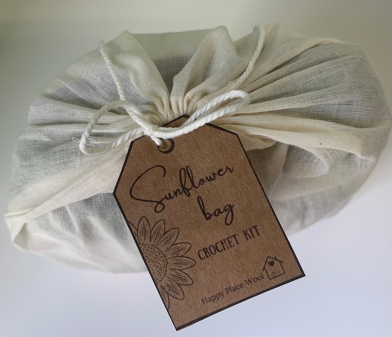 May include: A brown paper tag with the text "Sunflower Bag Crochet Kit" and the logo "Happy Place Wool" is tied to a white muslin bag.