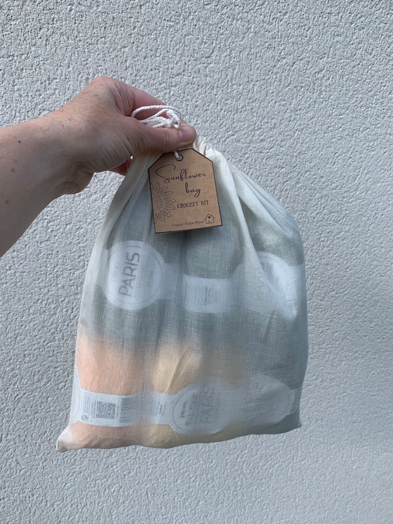 May include: A white cotton drawstring bag with a brown tag that says "Sunflower Bag Crochet Kit Happy Place Wool". The bag contains yarn skeins.