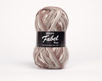 May include: A ball of Drops Fabel Print yarn in shades of brown, gray, and white. The yarn is superwash treated sock wool. The label reads "DROPS Fabel Print". The yarn is tightly wound and ready for knitting or crocheting projects.