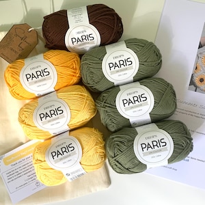 May include: A set of yarn for crocheting a sunflower bag. The yarn is in shades of yellow, green, and brown. The yarn is labeled "DROPS PARIS UN COLOUR 100% Cotton".
