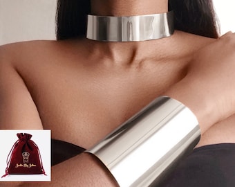 Puede incluir: Un collar choker plateado y un brazalete de puño plateado. Las joyas son reflectantes y tienen un acabado liso y pulido.