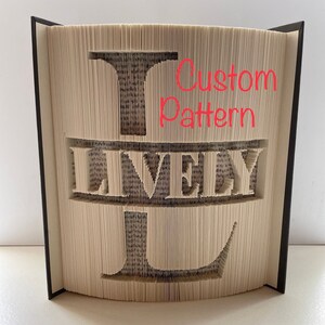 May include: A book with pages carved to display the letter "L" and the word "LIVELY". The book has a black spine and the text "Custom Pattern" is written in red. The pages are beige and the carved letters reveal the text within.