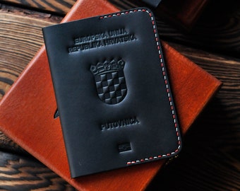 Può includere: Due custodie per passaporto in pelle nera con cuciture rosse e bianche. Le custodie presentano lo stemma croato e il testo "EUROPSKA UNIJA REPUBLIKA HRVATSKA" e "PUTOVNICA".