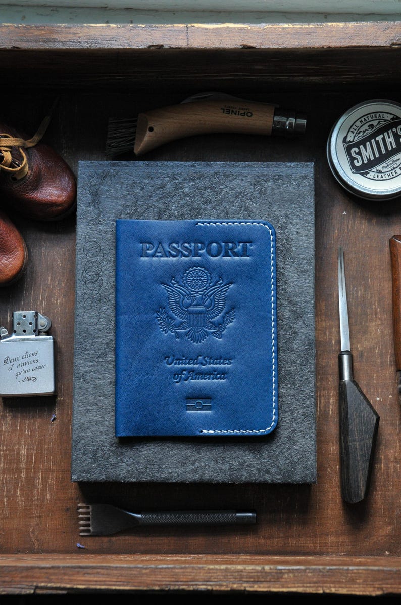 May include: A blue leather passport holder with the words "PASSPORT", "United States of America", and an embossed image of the American eagle.