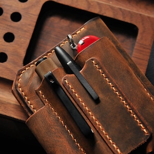 May include: A brown leather carrying case with multiple pockets for pens and a small multi-tool. The case has a distressed look and is stitched with brown thread.