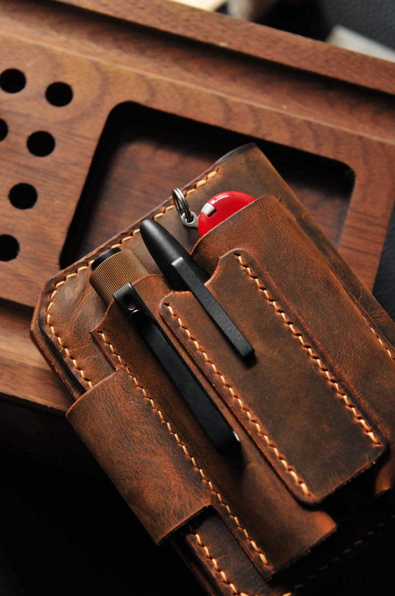May include: A brown leather carrying case with multiple pockets for pens and a small multi-tool. The case has a distressed look and is stitched with brown thread.