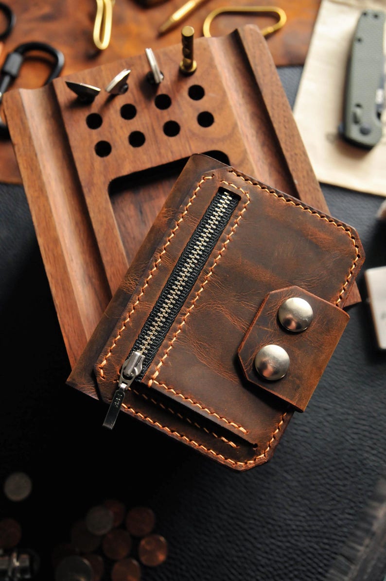 May include: A brown leather wallet with a zippered pocket and two silver metal snaps. The wallet has a distressed look and is made of high-quality leather.