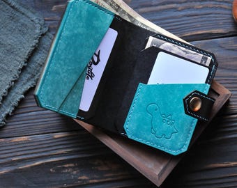 May include: A teal and black leather wallet with a dinosaur design and the word "Doxable" embossed on the front. The wallet is open and has cash and a card inside.