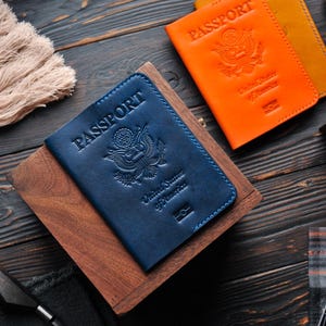 May include: Two leather passport covers, one blue and one orange, with the words "PASSPORT" embossed on the front. Both covers feature the United States of America seal.