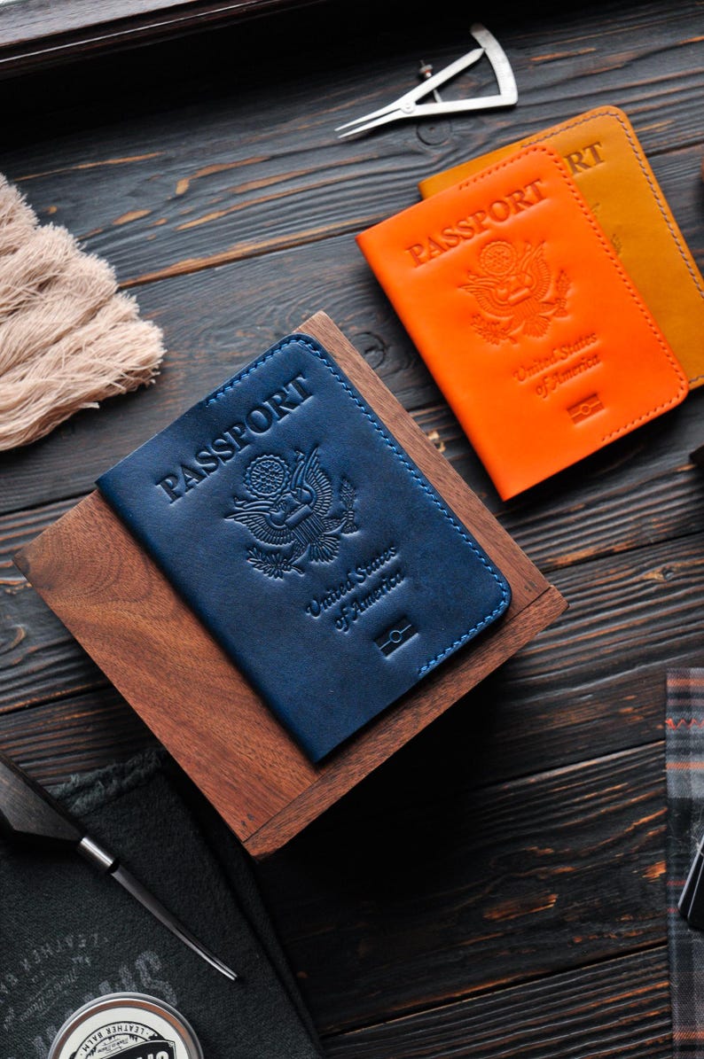 May include: Two leather passport covers, one blue and one orange, with the words "PASSPORT" embossed on the front. Both covers feature the United States of America seal.