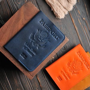 May include: Two passport covers, one blue and one orange, with the words "PASSPORT" embossed on the front. Both covers feature the United States seal.