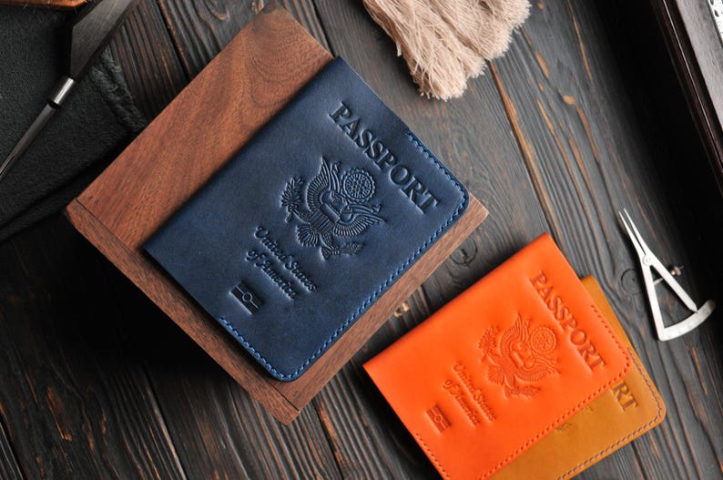 May include: Two passport covers, one blue and one orange, with the words "PASSPORT" embossed on the front. Both covers feature the United States seal.