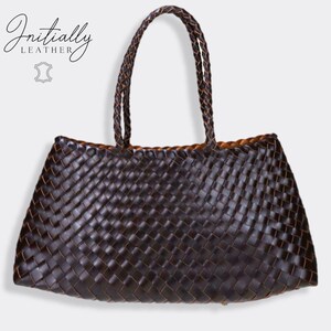 May include: A dark brown woven leather tote bag with braided handles. The bag has a rectangular shape with a wide opening and a contrasting tan interior. The brand name "Initially Leather" is displayed in the upper left corner.