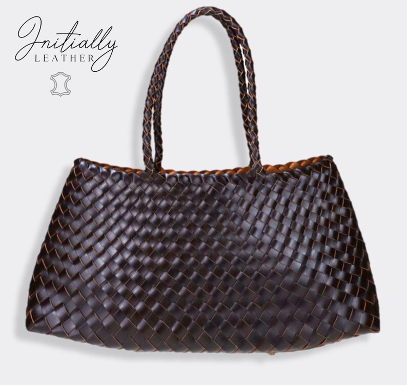 May include: A dark brown woven leather tote bag with braided handles. The bag has a rectangular shape with a wide opening and a contrasting tan interior. The brand name "Initially Leather" is displayed in the upper left corner.