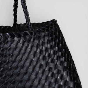 May include: Black woven tote bag with braided handles. The bag features a basket weave design, with a structured shape. The handles are also braided. The bag is made of a durable material.