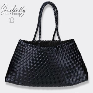 May include: A black woven leather tote bag with braided handles. The bag has a trapezoid shape and a textured surface. The brand name "Initially Leather" is displayed in cursive script on the upper left corner.