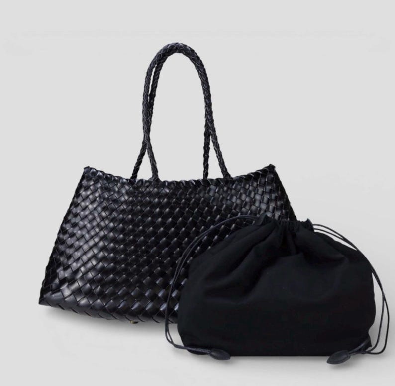 May include: A black woven tote bag with braided handles and a matching drawstring bag. The tote bag has a rectangular shape with a woven pattern. The drawstring bag is made of a soft, dark fabric.