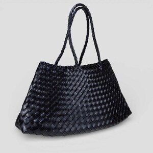 May include: Black woven tote bag with braided handles. The bag features a trapezoid shape and a tightly woven pattern. The handles are also black and braided, providing a cohesive design. The bag is suitable for carrying various items.