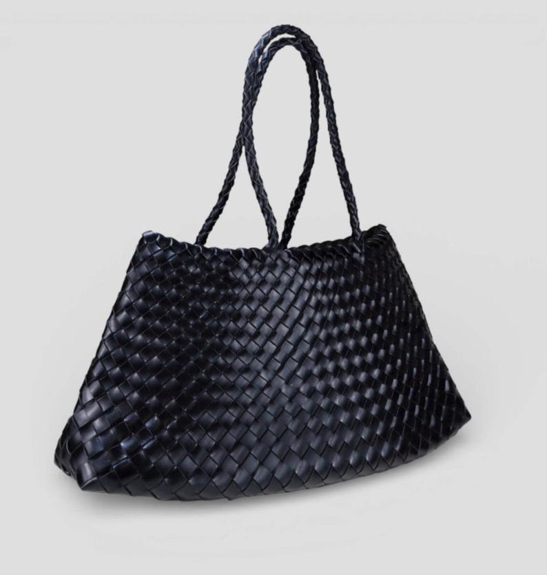 May include: Black woven tote bag with braided handles. The bag features a trapezoid shape and a tightly woven pattern. The handles are also black and braided, providing a cohesive design. The bag is suitable for carrying various items.