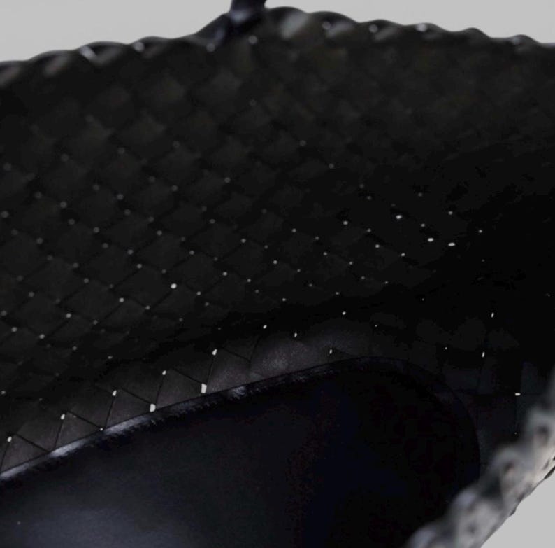 May include: Close-up of a black woven tote bag. The bag's interior is visible, showcasing a dark, smooth lining. The woven pattern creates a textured surface, with small gaps between the woven material.